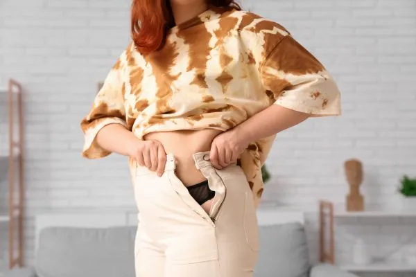 Image of woman trying to do her trousers up after pregnancy weight gain Blackburn